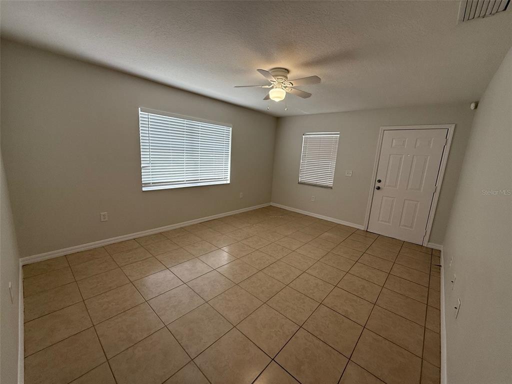 An empty room features beige tile flooring, light-colored walls, a ceiling fan, and two windows — 1802 MARTIN LUTHER KING AVENUE E, BRADENTON, FL