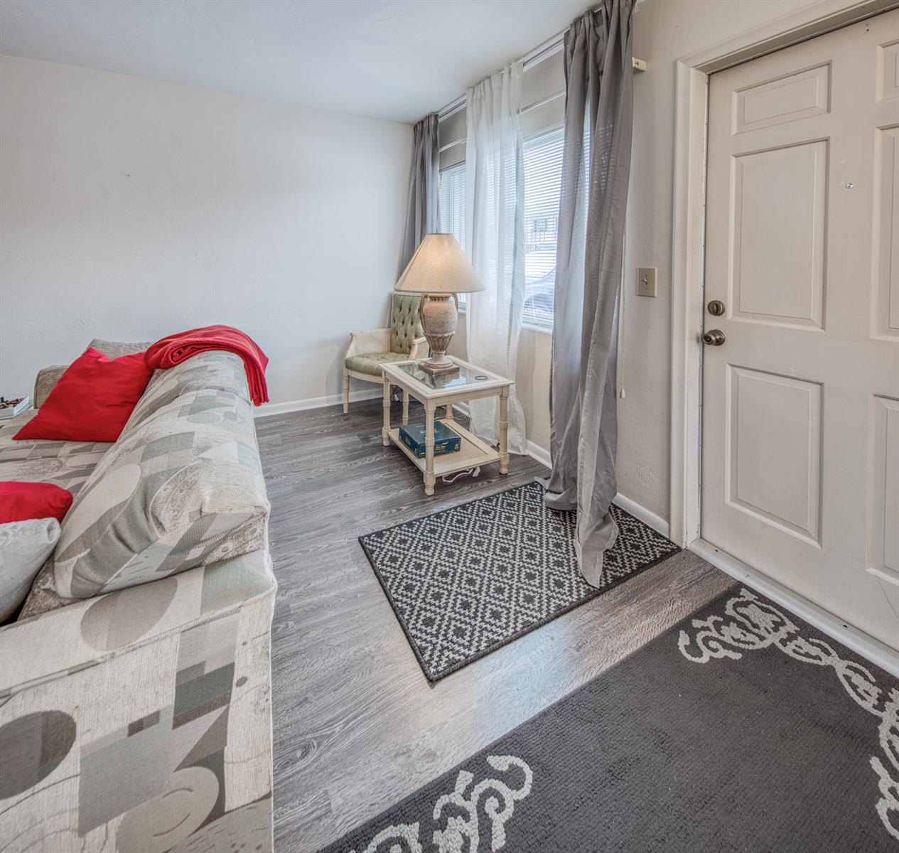 A living room features gray wood-look flooring, a patterned sofa, an accent chair, and curtains — 3040 Lake Osborne Drive # 106, FL 33461, FL
