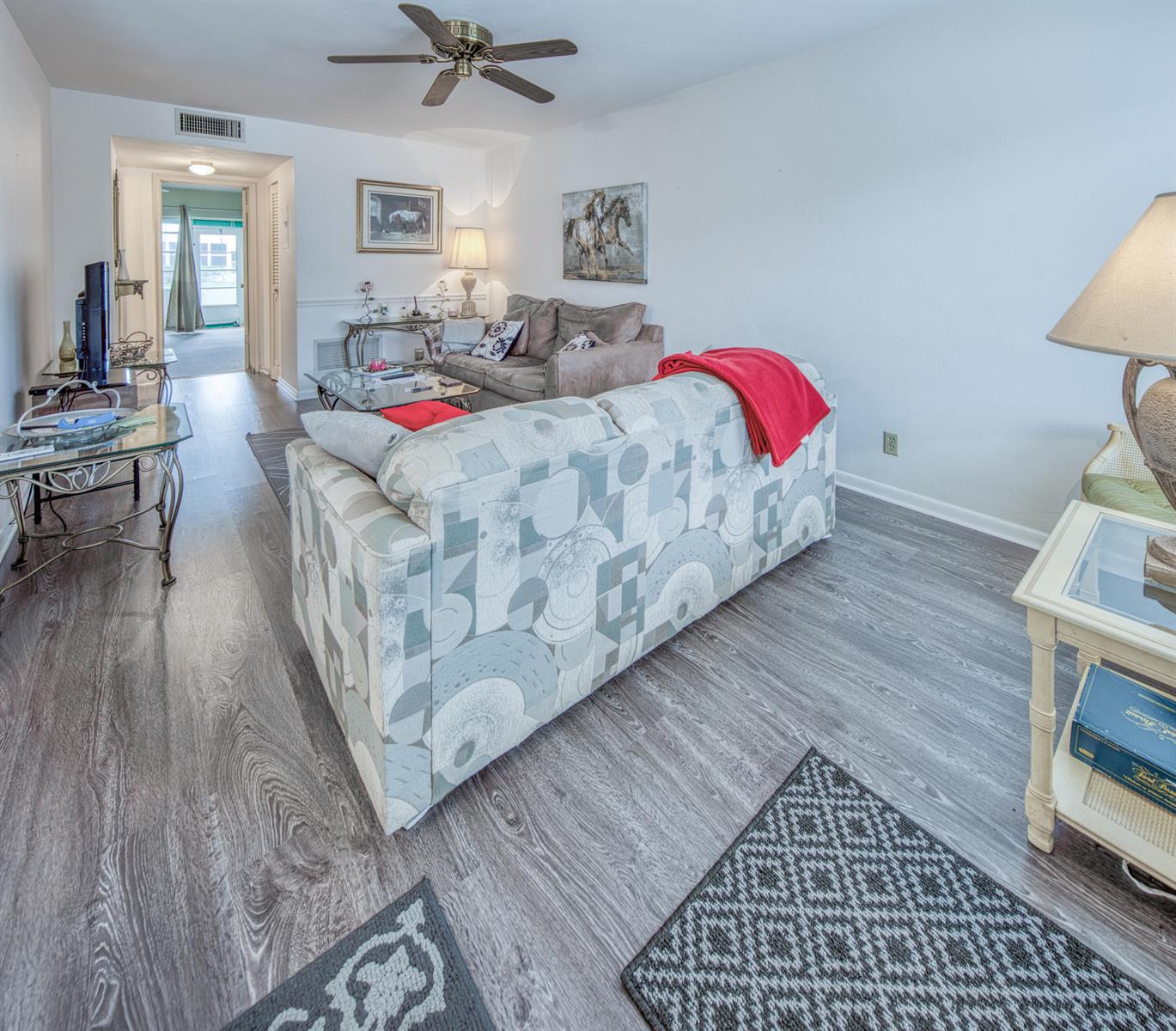 A living room features a patterned sofa, wood-look flooring, and a ceiling fan — 3040 Lake Osborne Drive # 106, FL 33461, FL