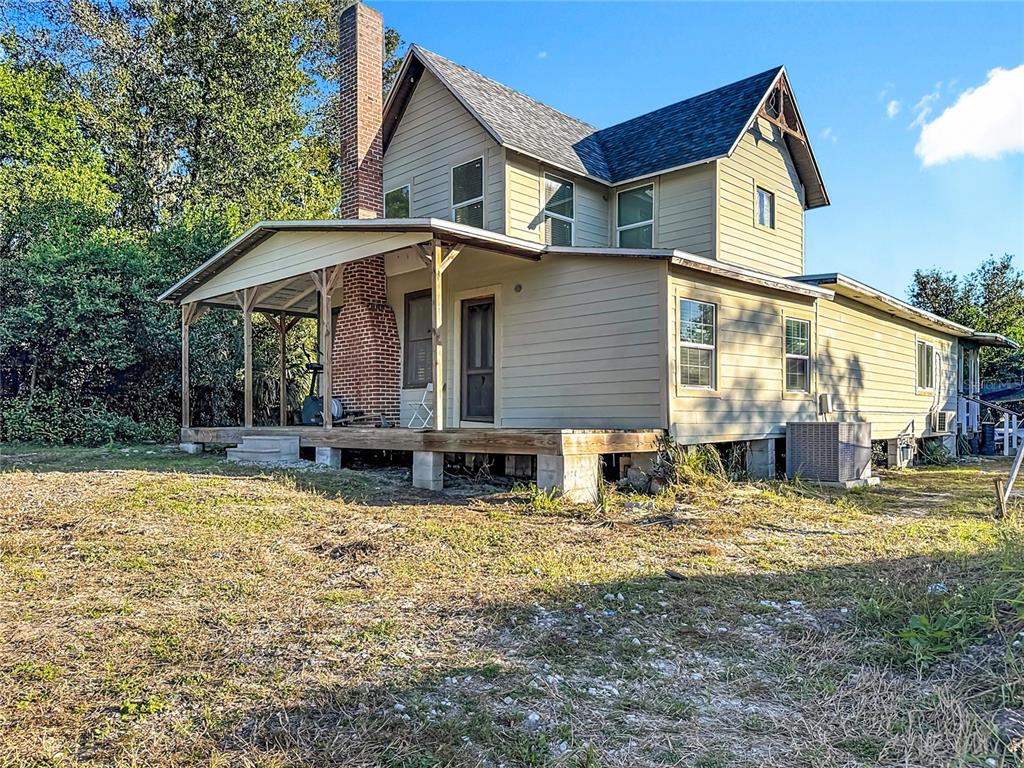 A two-story house with tan siding, a brick chimney, and a covered wooden deck — 7717 CLARCONA OCOEE ROAD, ORLANDO, FL