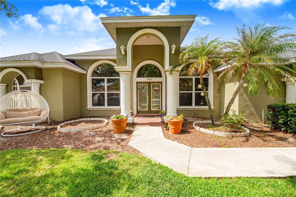 The exterior of a single-story house features a covered entryway with columns and arched windows — 445 TALAMONE DRIVE, WINTER HAVEN, FL