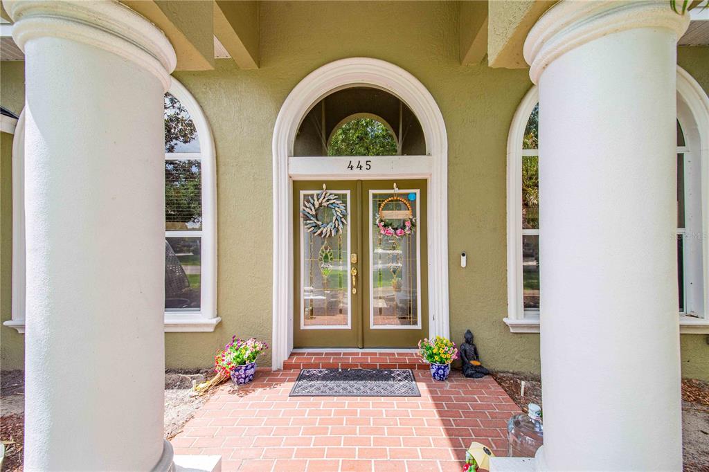 The front entrance features double glass doors with wreaths between two large white columns — 445 TALAMONE DRIVE, WINTER HAVEN, FL