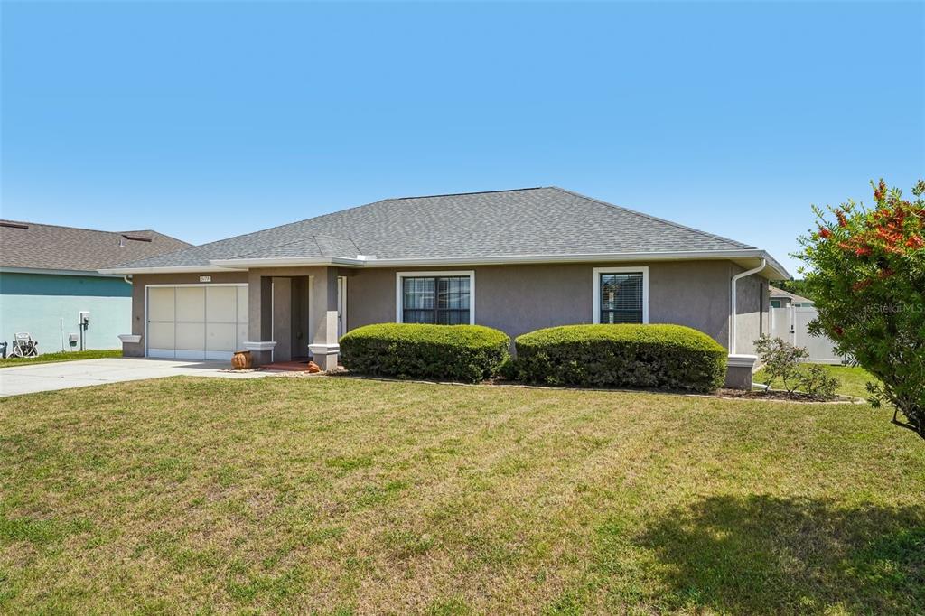 A single-story house with a gray stucco exterior, a two-car garage, and manicured landscaping — 5179 SE 92ND STREET, OCALA, FL