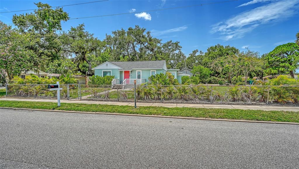 A light green single-story house with a bright red front door sits behind a chain-link fence — 1507 10TH AVENUE W, PALMETTO, FL
