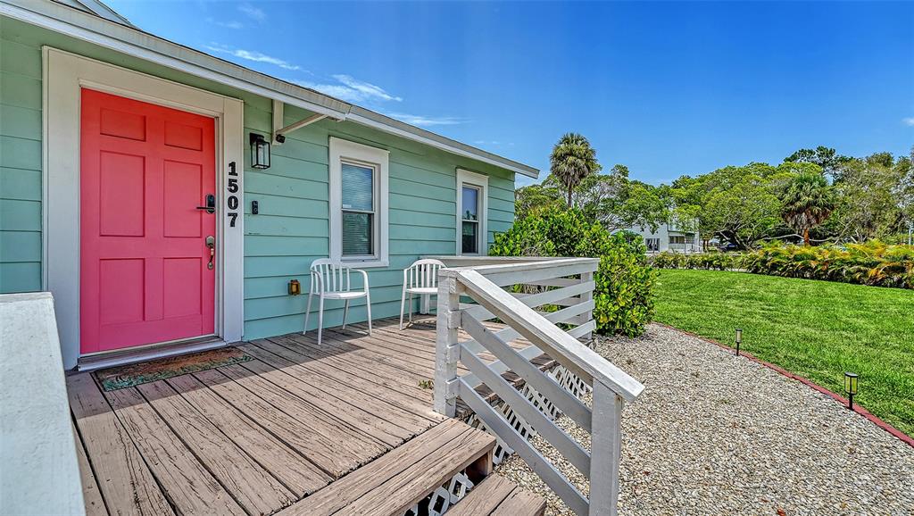 A light green house features a bright pink front door and a wooden porch deck — 1507 10TH AVENUE W, PALMETTO, FL