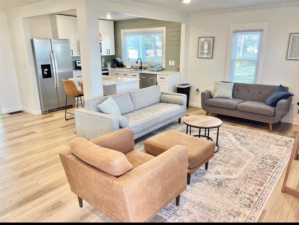 An open-concept living room features light wood flooring, a grey sofa, and a leather armchair — 1507 10TH AVENUE W, PALMETTO, FL