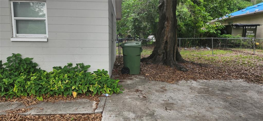 A green trash bin sits on a concrete driveway next to a house and tree — 8501 N MULBERRY STREET UNIT B, TAMPA, FL