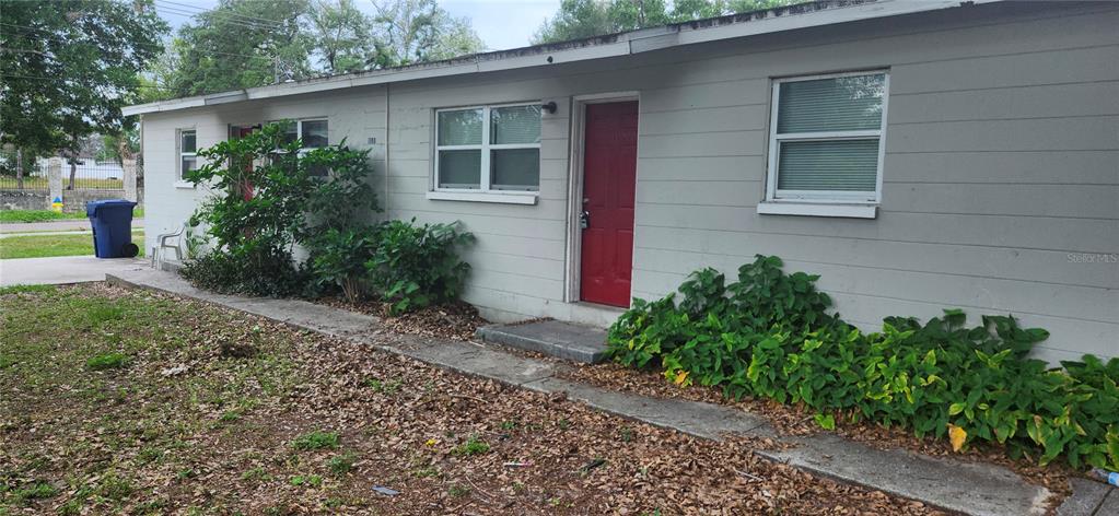 A single-story building exterior features light gray siding, a red door, and green landscaping — 8501 N MULBERRY STREET UNIT B, TAMPA, FL