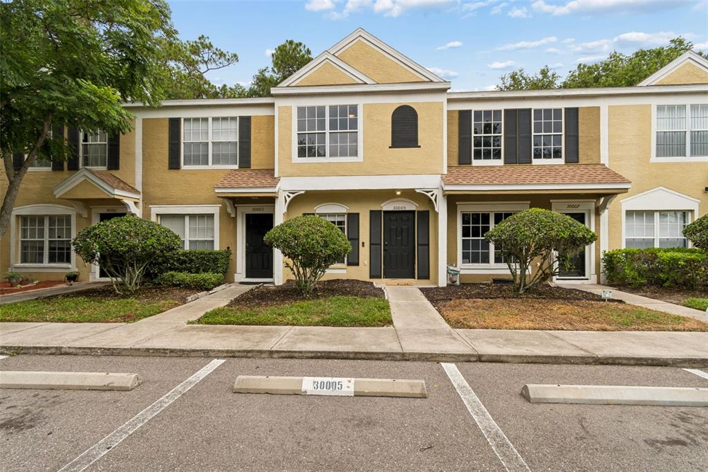 A two-story townhouse exterior features tan stucco walls, dark shutters, and a paved parking area — 30005 GRANDA HILLS COURT, WESLEY CHAPEL, FL