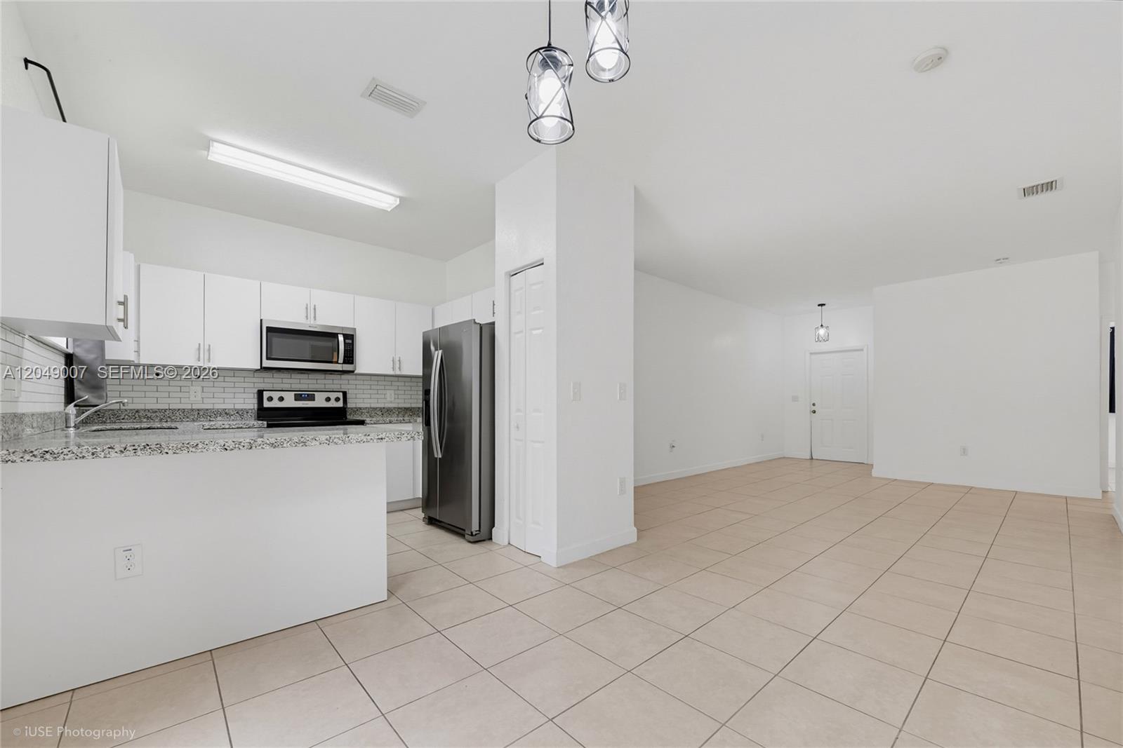 A kitchen with white cabinets and granite countertops opens into a tiled living area — 2630 NE 3rd Dr # 204, Homestead FL 33033, HOMESTEAD, FL