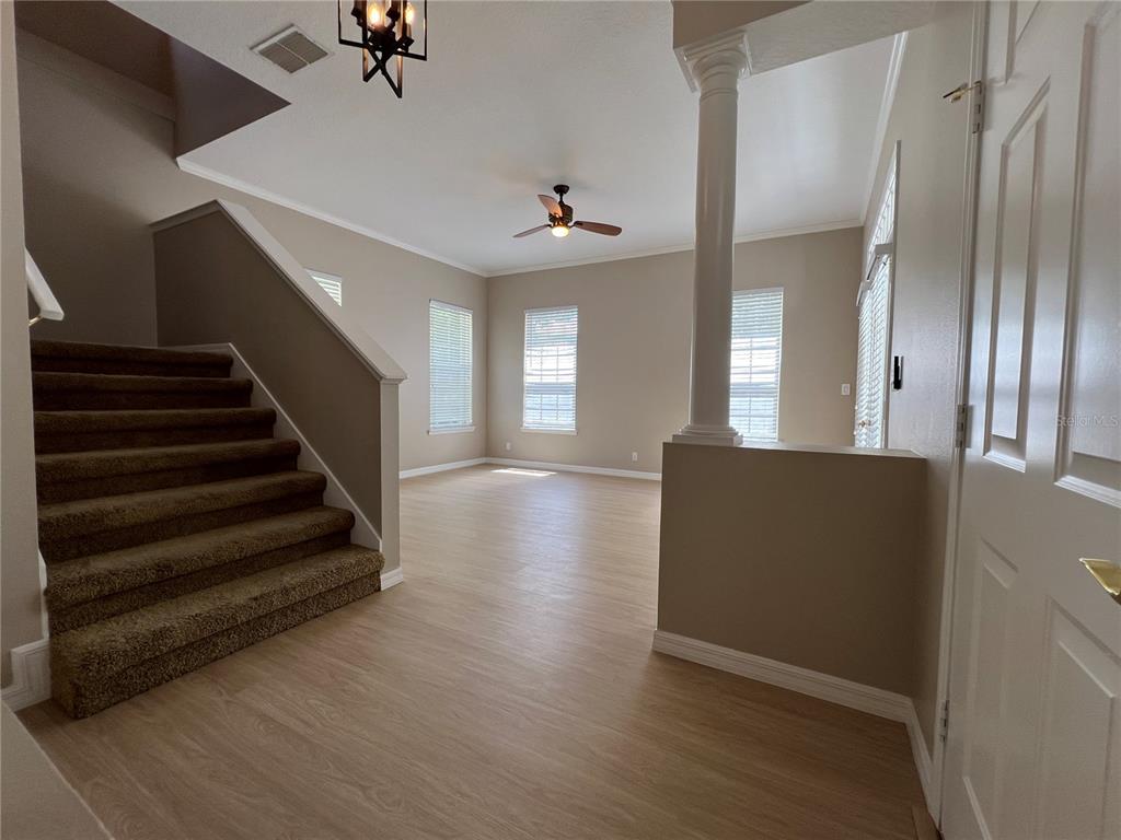 An entryway with brown carpeted stairs, light wood-look flooring, and a white support column — 502 GREENBRIER AVENUE, KISSIMMEE, FL