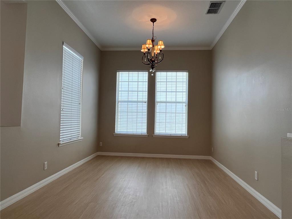 An empty room with light wood-look flooring, beige walls, three windows, and a chandelier — 502 GREENBRIER AVENUE, KISSIMMEE, FL
