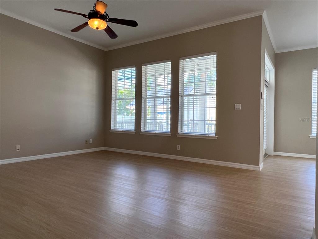 An empty room with light wood-look flooring, beige walls, three windows, and a ceiling fan — 502 GREENBRIER AVENUE, KISSIMMEE, FL