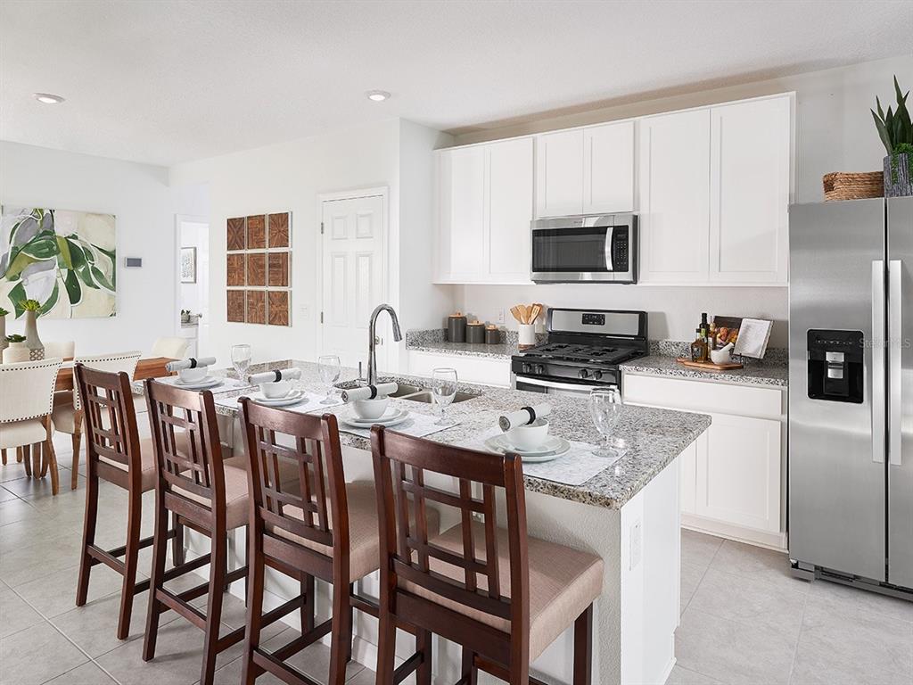A kitchen features white cabinets, granite countertops, stainless steel appliances, and a breakfast bar island — 102 WANDERING CREEK WAY, PALM COAST, FL