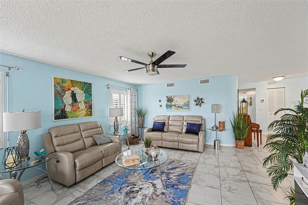 A living room with light blue walls, tile floors, two leather sofas, and a ceiling fan — 8198 TERRACE GARDEN DRIVE N UNIT 411, ST PETERSBURG, FL