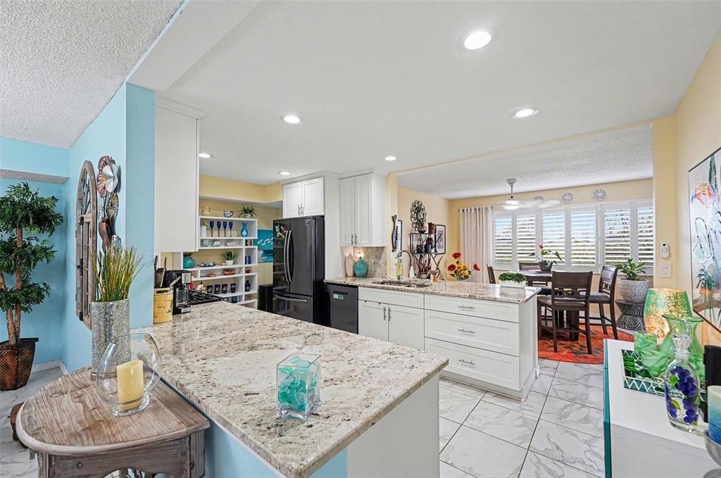 A kitchen features white cabinets, granite countertops, a center island, and an adjacent dining area — 8198 TERRACE GARDEN DRIVE N UNIT 411, ST PETERSBURG, FL