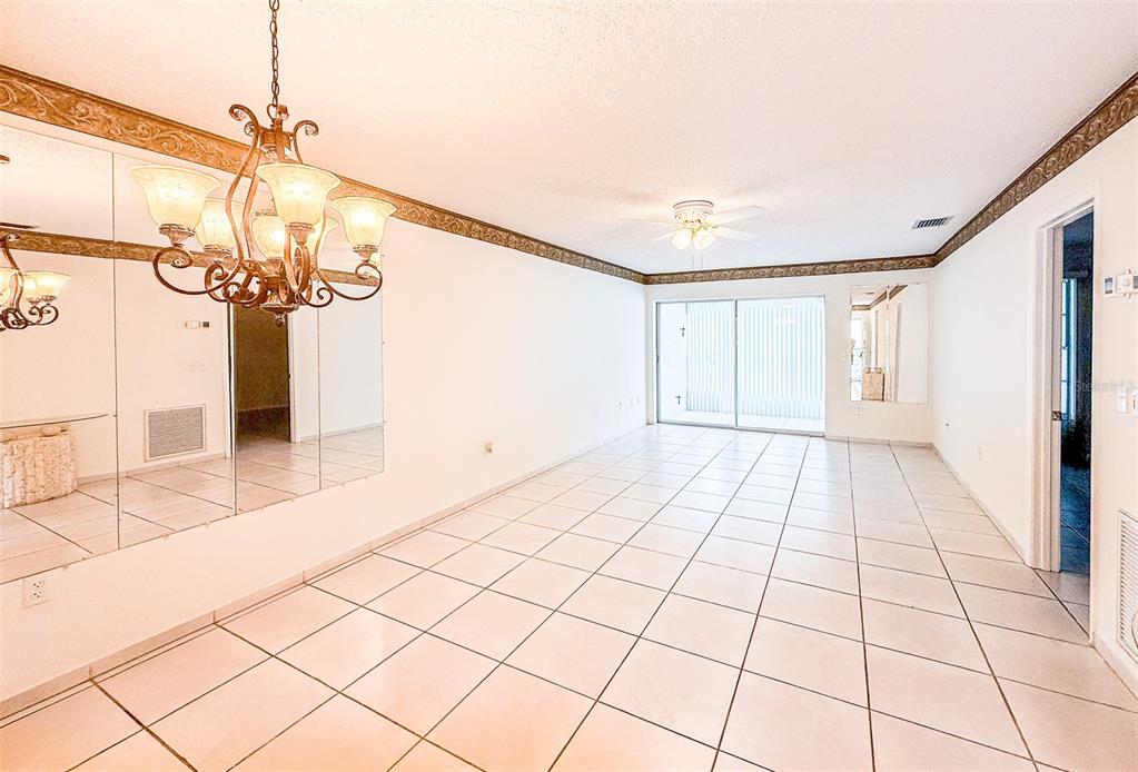 A dining room with white tile floors, a decorative chandelier, and a mirrored accent wall — 2604 WOODGATE LANE UNIT J6, SARASOTA, FL