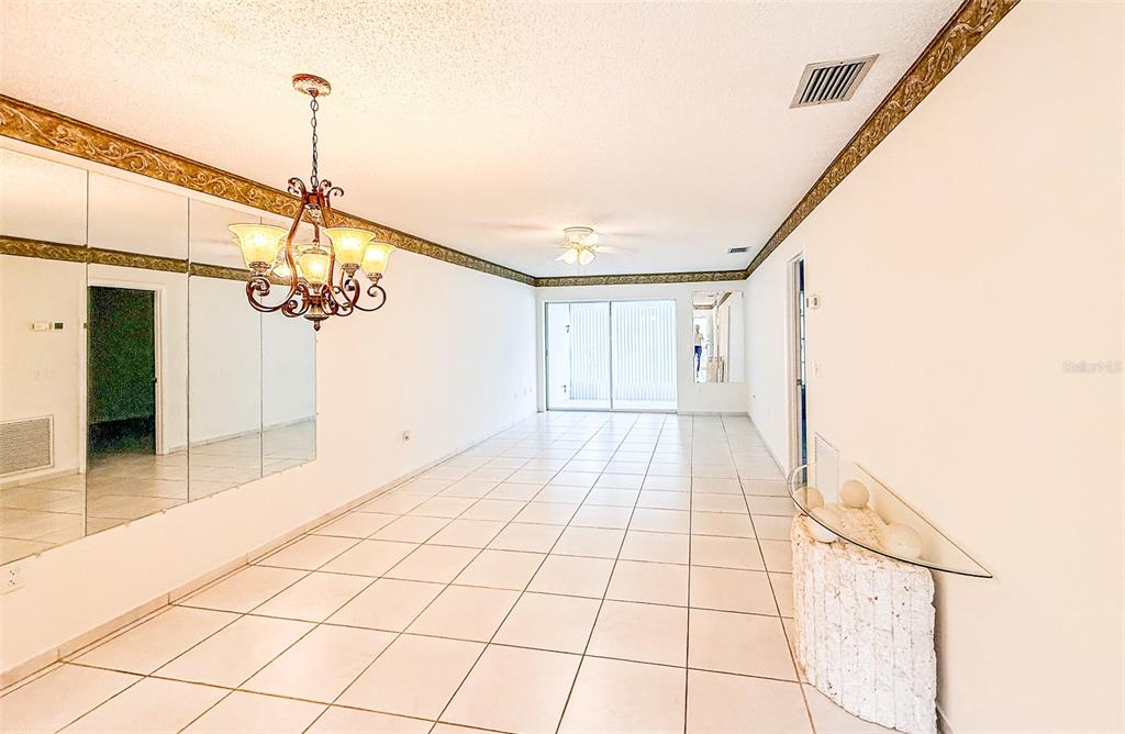 A bright, tiled dining room features a large chandelier, mirrored walls, and sliding glass doors — 2604 WOODGATE LANE UNIT J6, SARASOTA, FL