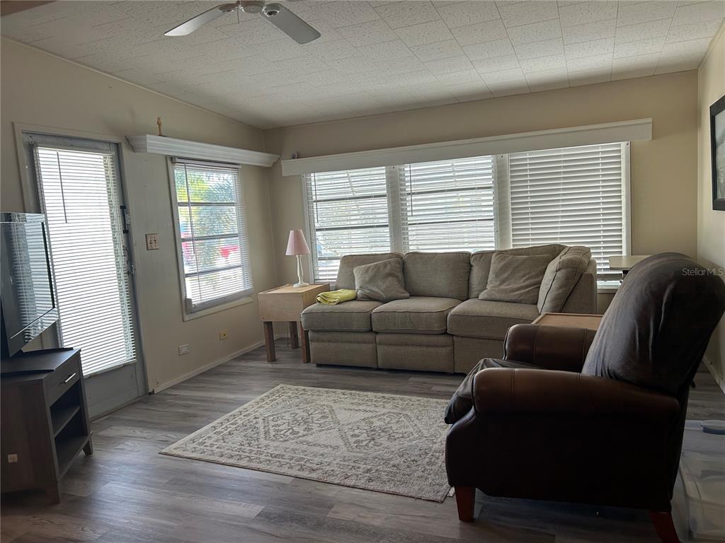 A living room features light wood-look flooring, a beige sofa, a brown armchair, and blinds — 5325 BOCA RATON AVENUE, SARASOTA, FL