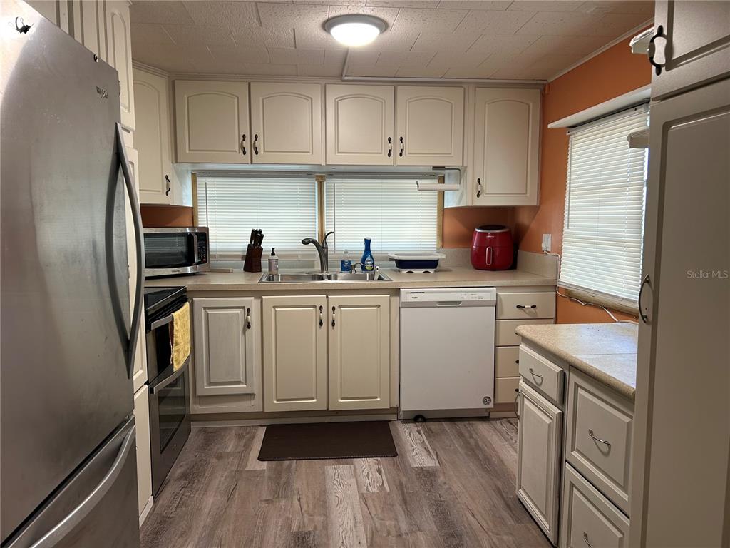 A kitchen features white cabinetry, stainless steel appliances, a double sink, and wood-look flooring — 5325 BOCA RATON AVENUE, SARASOTA, FL