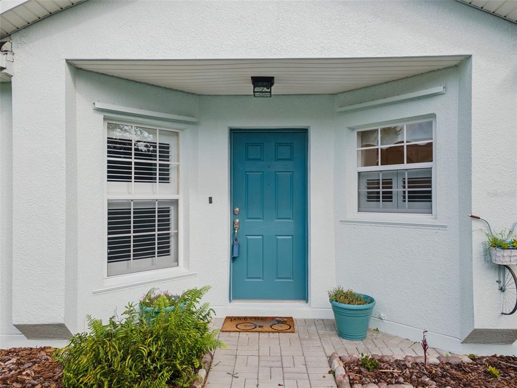 A teal front door is centered between two windows on a light-colored stucco house exterior — 205 BELL TOWER CROSSING WEST, POINCIANA, FL