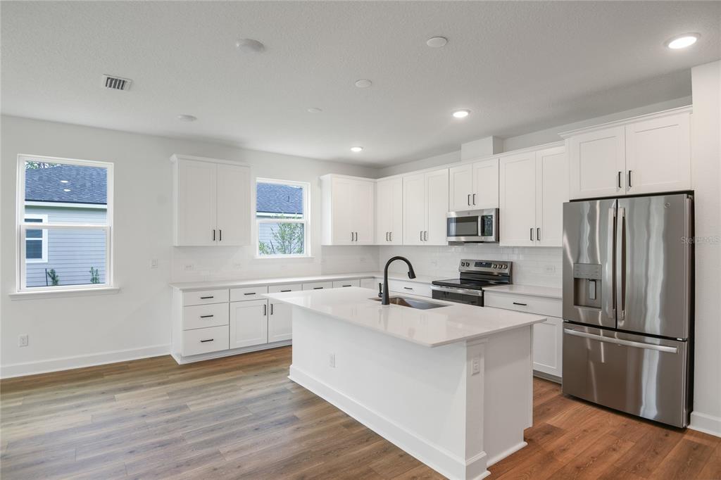 A modern kitchen features white cabinets, stainless steel appliances, a center island, and wood flooring — 39 PONCE PRESERVE DRIVE, PALM COAST, FL
