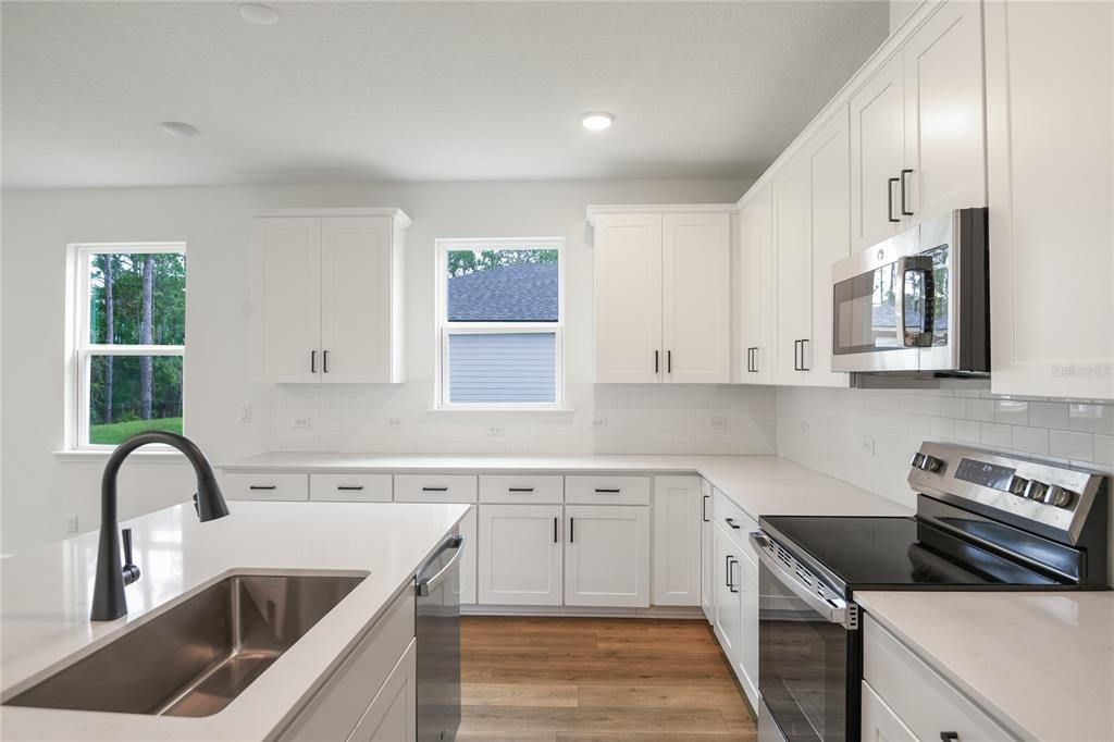 A modern kitchen features white cabinets, stainless steel appliances, a kitchen island, and wood flooring — 39 PONCE PRESERVE DRIVE, PALM COAST, FL