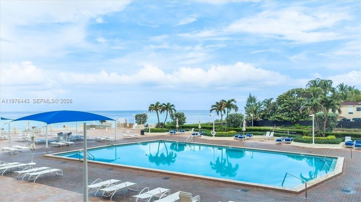 A rectangular swimming pool sits on a brick patio overlooking the ocean under blue skies — 3180 S Ocean Dr # 1018, Hallandale Beach FL 33009, HALLANDALE BEACH, FL