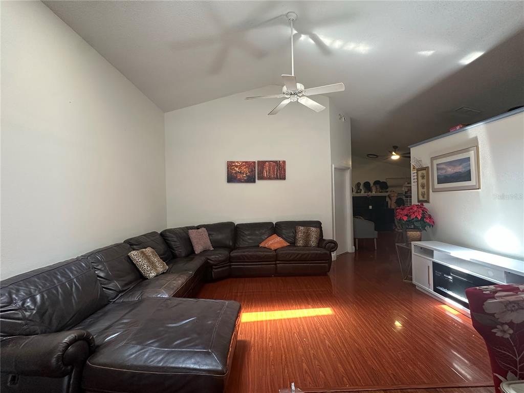 A living room features a large brown sectional sofa, hardwood floors, and a ceiling fan — 1409 WOODFIELD OAKS DRIVE, APOPKA, FL