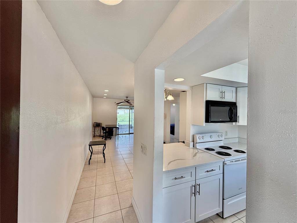 A view from a kitchen looking into a tiled living area with a sliding glass door — 9605 EASTFIELD ROAD UNIT 9605, THONOTOSASSA, FL