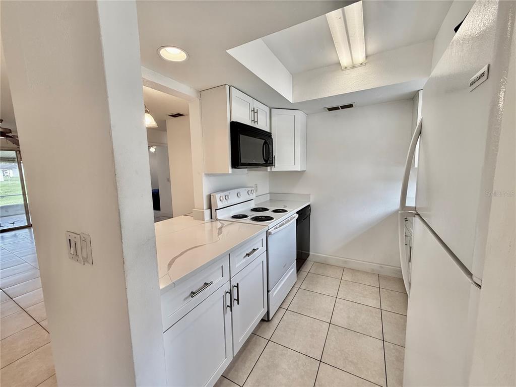 A kitchen features white cabinets, quartz countertops, a white stove, and a white refrigerator — 9605 EASTFIELD ROAD UNIT 9605, THONOTOSASSA, FL