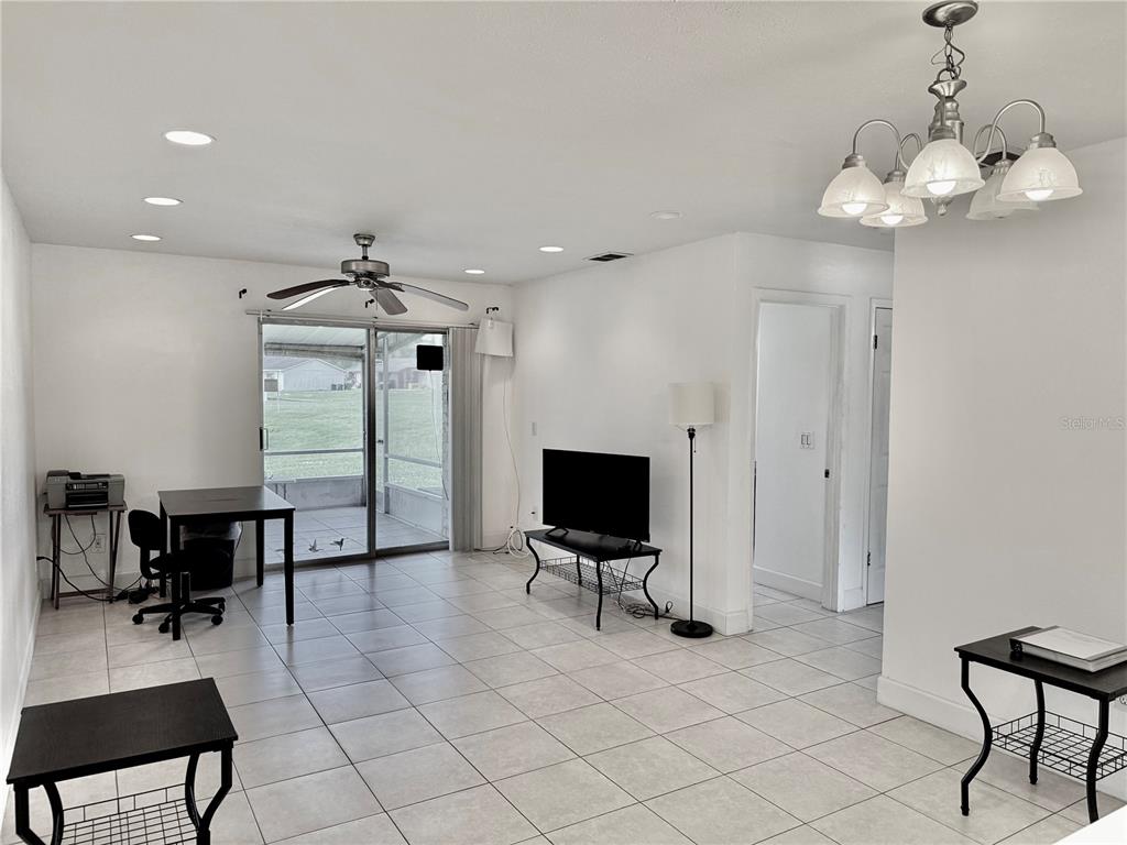 A bright living room features white tile floors, a ceiling fan, and a sliding glass door — 9605 EASTFIELD ROAD UNIT 9605, THONOTOSASSA, FL