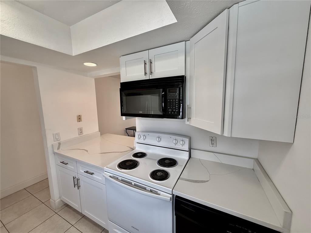 A kitchen features white cabinets, a black microwave, a white electric stove, and quartz countertops — 9605 EASTFIELD ROAD UNIT 9605, THONOTOSASSA, FL