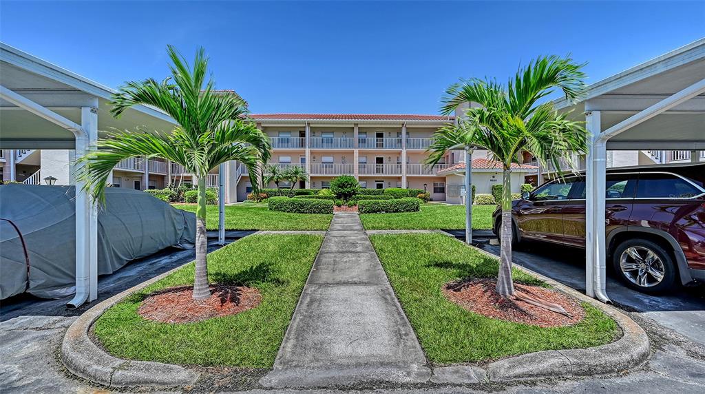 A sidewalk leads to a three-story apartment building between two covered parking areas — 6505 STONE RIVER ROAD UNIT 209, BRADENTON, FL