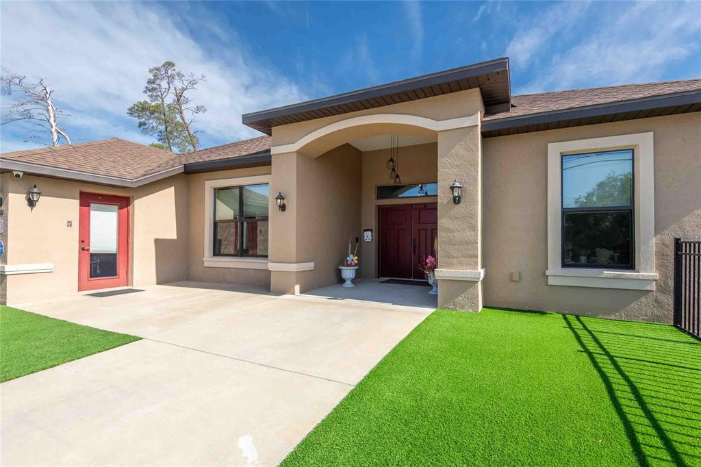 A tan stucco house exterior features a covered entryway with double doors and artificial turf — 13031 PARTRIDGE STREET, SPRING HILL, FL