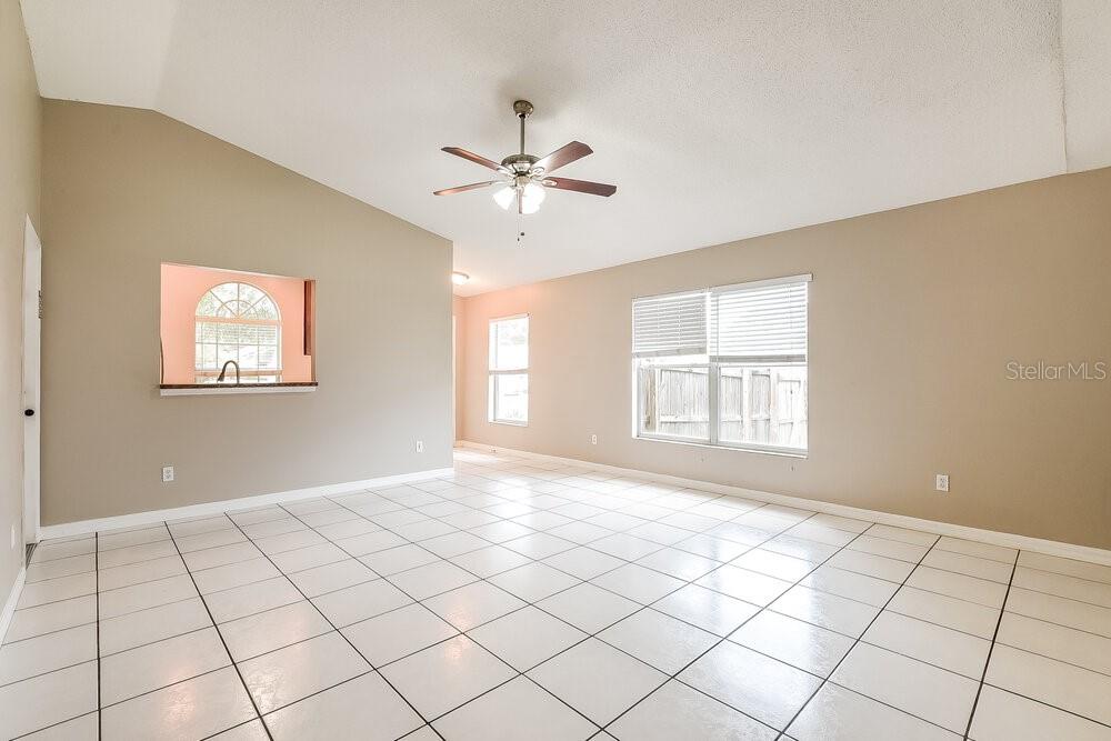 A spacious living room features light-colored tile flooring, beige walls, and a vaulted ceiling — 145 BURNSED PLACE, OVIEDO, FL