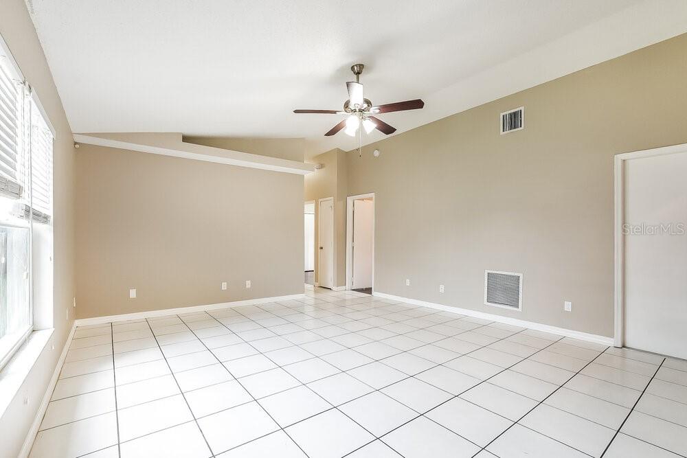 An empty room with white tile floors, beige walls, and a vaulted ceiling with a fan — 145 BURNSED PLACE, OVIEDO, FL
