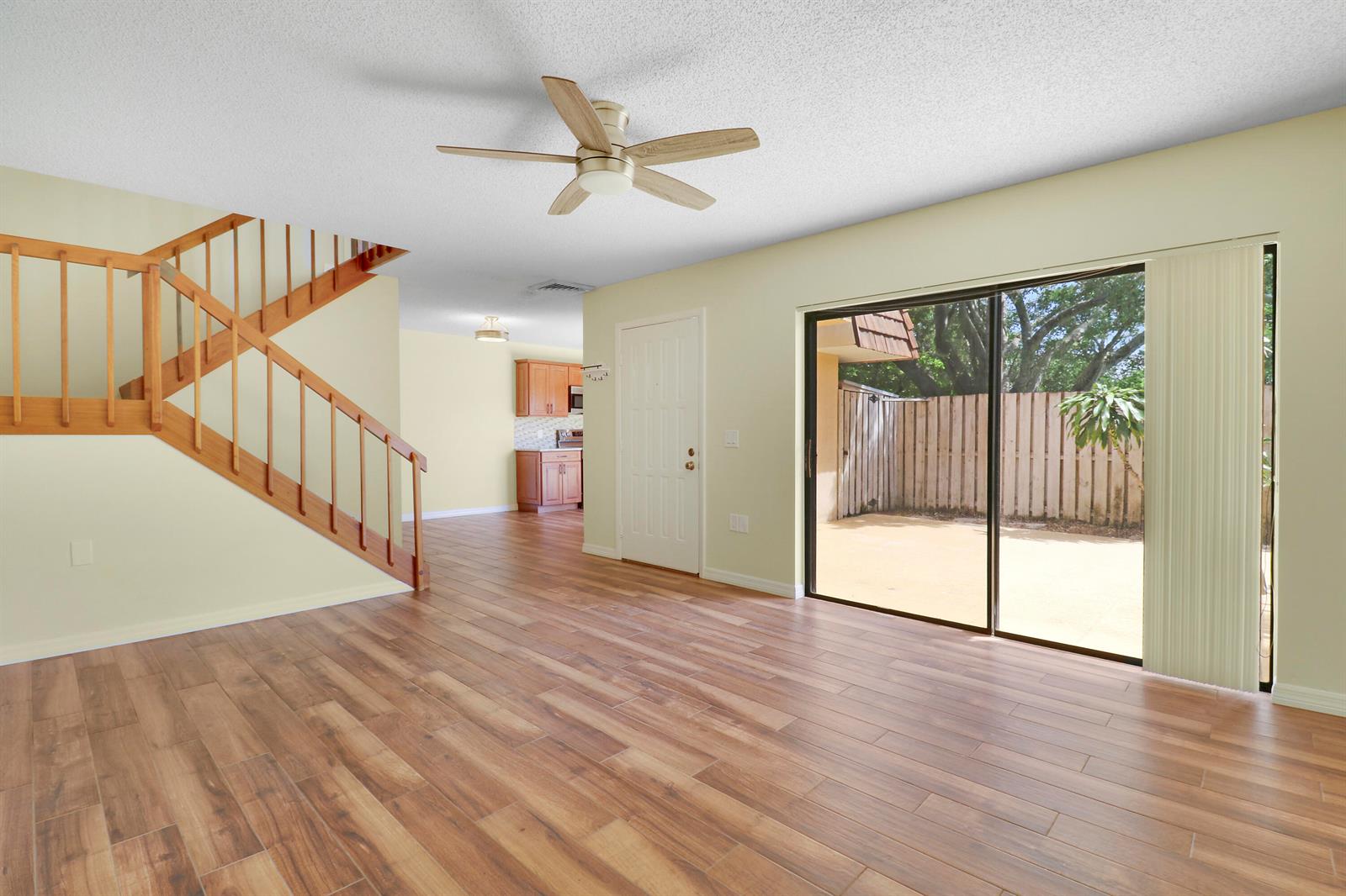 An empty living room features wood-look tile flooring, a wooden staircase, and a sliding glass door — 1511 15th Lane Bldg 65, FL 33463, FL