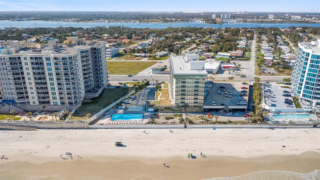 An aerial view shows beachfront high-rise condominiums with swimming pools and a parking lot — 1909 S ATLANTIC AVENUE UNIT 717, DAYTONA BEACH, FL