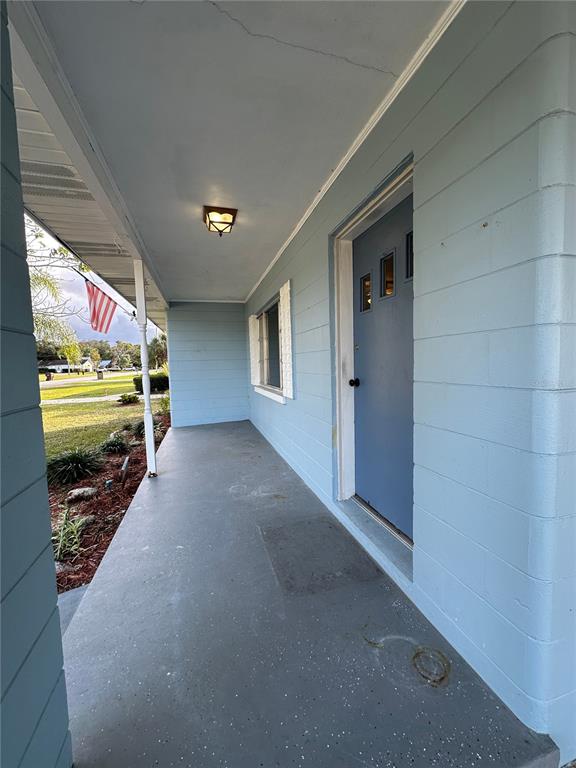 A covered porch with a blue door, light fixture, and concrete floor overlooks a yard — 1400 CAROLINA AVENUE, ST CLOUD, FL