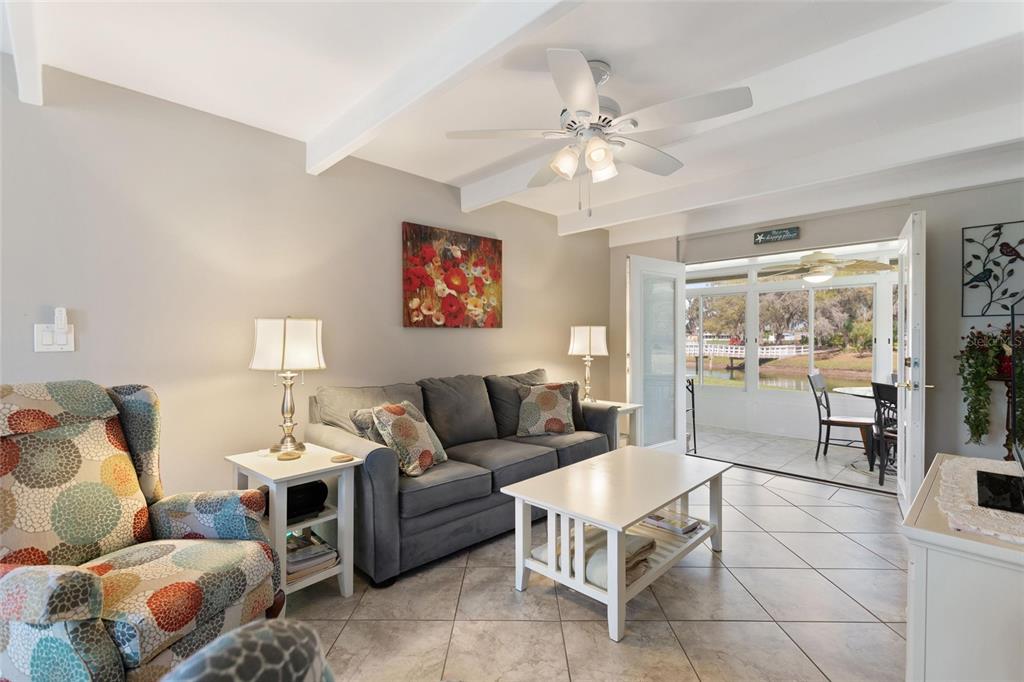 A living room with tile floors, a gray sofa, patterned armchair, and a sunroom view — 1919 CLUB CIRCLE, LAKE WALES, FL