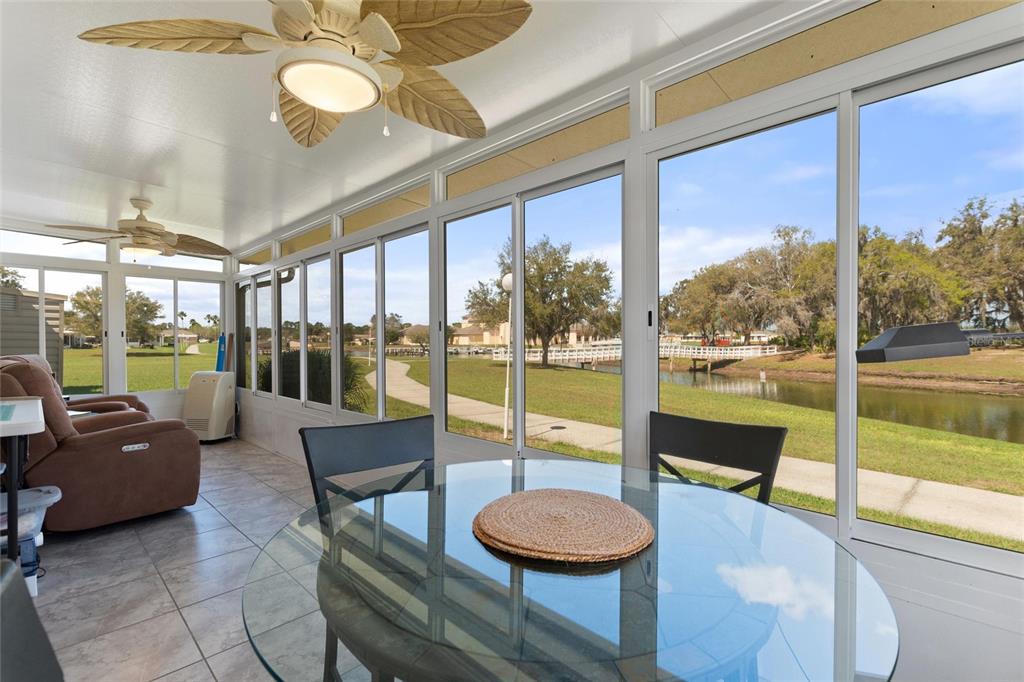 A sunroom with tile floors, a glass dining table, and views of a pond outside — 1919 CLUB CIRCLE, LAKE WALES, FL