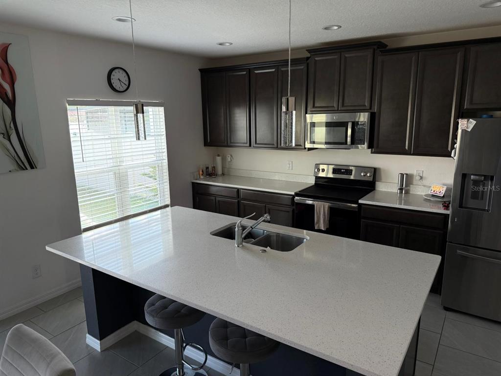 A kitchen features dark cabinetry, white countertops, a central island with seating, and stainless appliances — 425 TORTUGAS STREET, HAINES CITY, FL