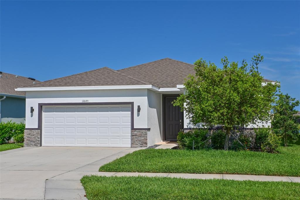 A single-story house with a white stucco exterior, stone accents, and a two-car garage — 12645 PROMENADE ESTATES BOULEVARD, SARASOTA, FL