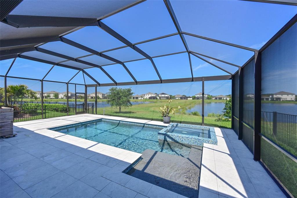 A screened-in patio features a swimming pool with an integrated spa overlooking a lake — 12645 PROMENADE ESTATES BOULEVARD, SARASOTA, FL
