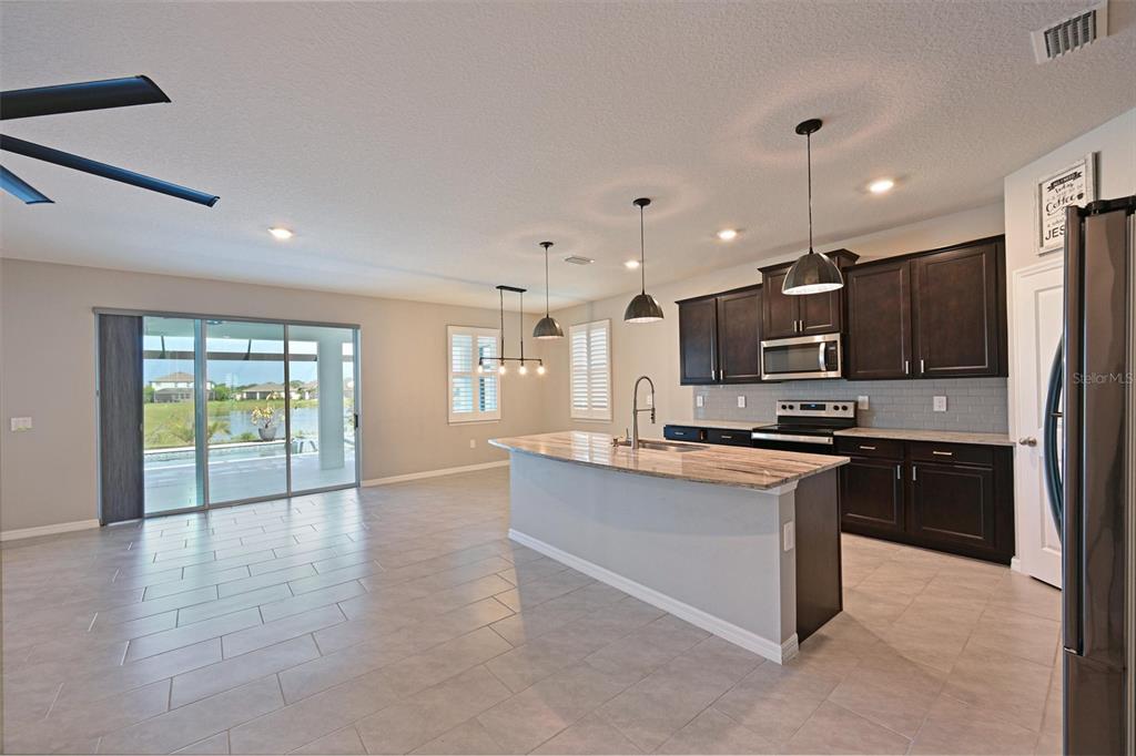 A kitchen with dark cabinets, a granite island, and a sliding door to a patio — 12645 PROMENADE ESTATES BOULEVARD, SARASOTA, FL