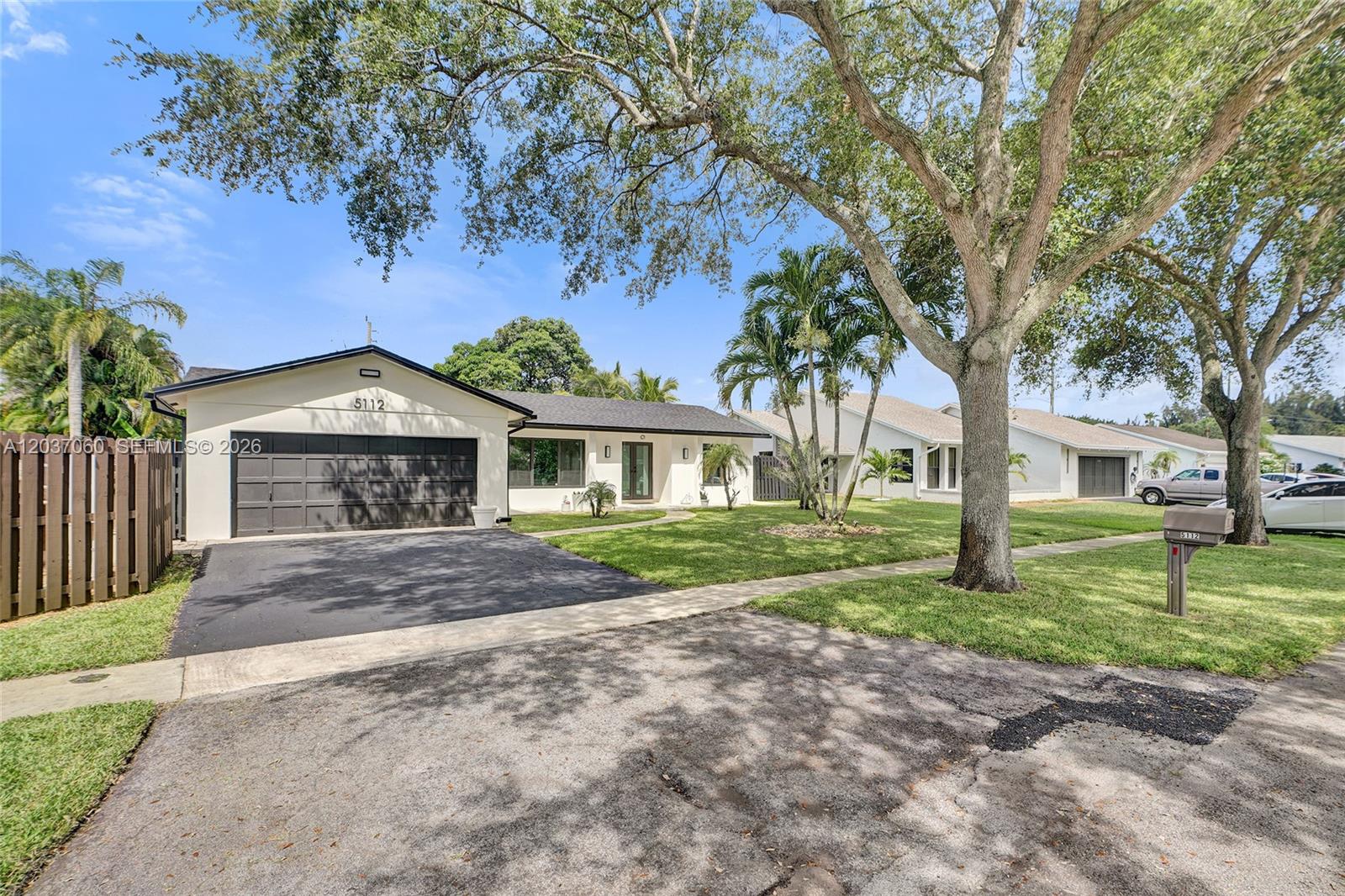 A single-story house with a dark garage door, a paved driveway, and large shade trees — 5112 SW 87th Ave, Cooper City FL 33328, COOPER CITY, FL