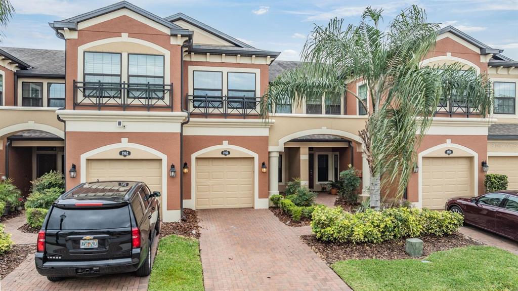 A row of three-story townhomes with stucco facades, arched entryways, and attached garages — 1958 MILKWEED TRACE, LUTZ, FL