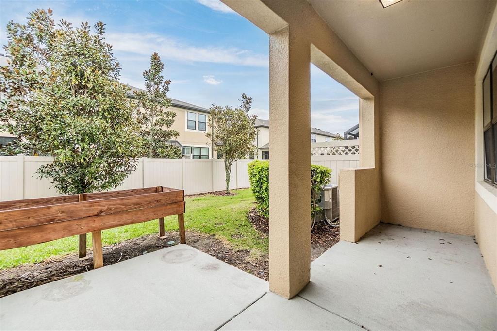 A covered concrete patio overlooks a small backyard with a wooden planter box and fence — 1958 MILKWEED TRACE, LUTZ, FL