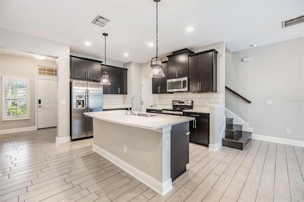 A kitchen with dark cabinets, stainless steel appliances, a center island, and light wood-look flooring — 1958 MILKWEED TRACE, LUTZ, FL